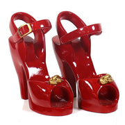 Red high-heeled shoe with an ornate Baroque-inspired gold accent and a classical ankle strap buckle design. Side View