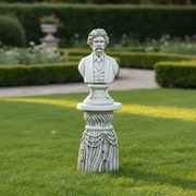 Bust of a distinguished man in classical attire atop an ornate, old world European pedestal with draped rope and tassel details. Side Angle