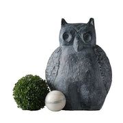 Owl statue with textured wings in an old world European style, flanked by a round topiary and a classical marble sphere.