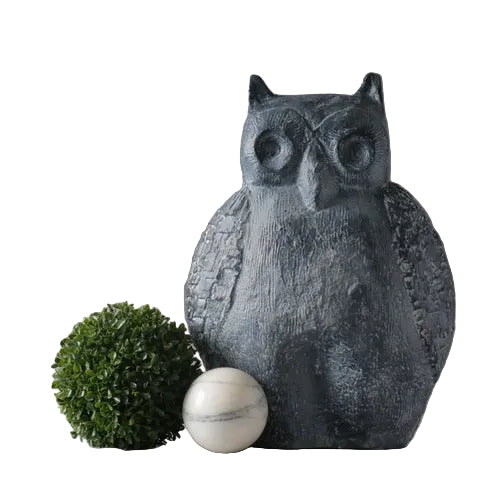 Owl statue with textured wings in an old world European style, flanked by a round topiary and a classical marble sphere.