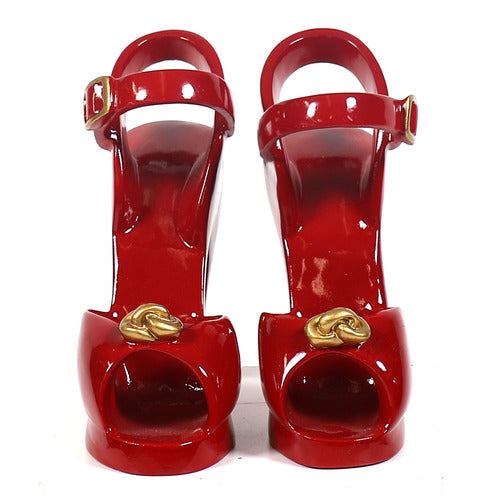 Red high-heeled shoe with an ornate Baroque-inspired gold accent and a classical ankle strap buckle design. Side Angle
